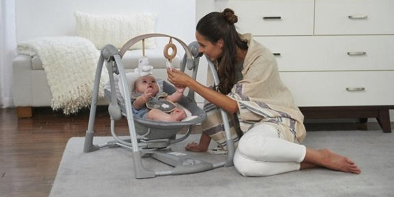 Woman sittng beside baby in Ingenuity swing