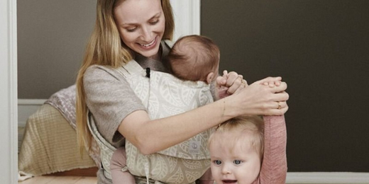 Woman Holding Toddlers Hand and Smiling While Wearing Stokke Limas Carrier With Newborn Inside