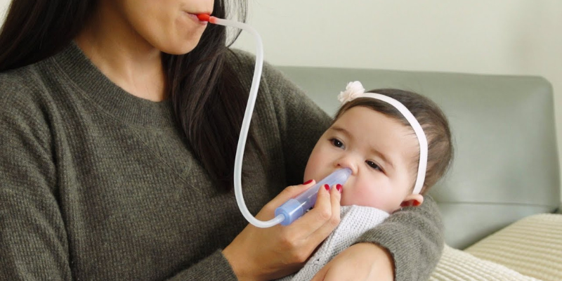Mother using the FridaBaby NoseFrida Nasal Aspirator on baby