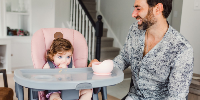 Dad feeding baby sitting in a Maxi Cosi Minla High Chair