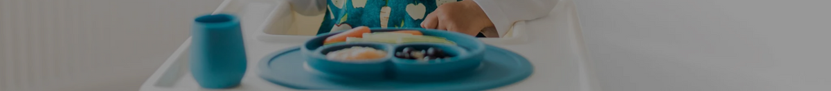 Child sitting in a high chair eating from an ezpz feeding place mat and silicone cup