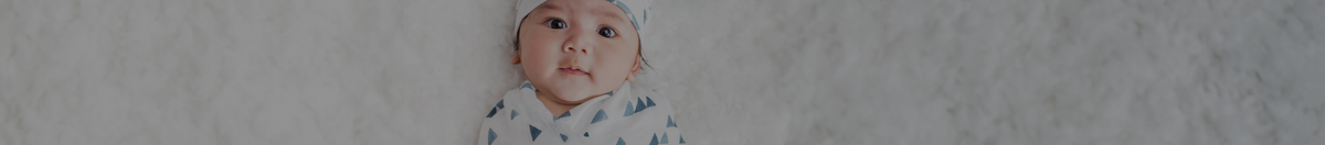 Baby wearing lulujo newborn hat and swaddle on carpet