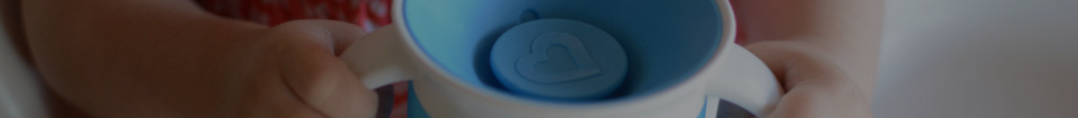 Closeup of a little girl sitting in her high chair holding a Munchkin 360 cup in blue with both handles