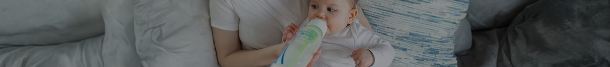 Mother sitting on the couch feeding newborn milk out of a Dr. Brown's baby bottle