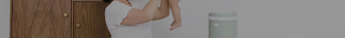 Women holding up child in a diaper with the UBBI diaper pail behind her in the nursery